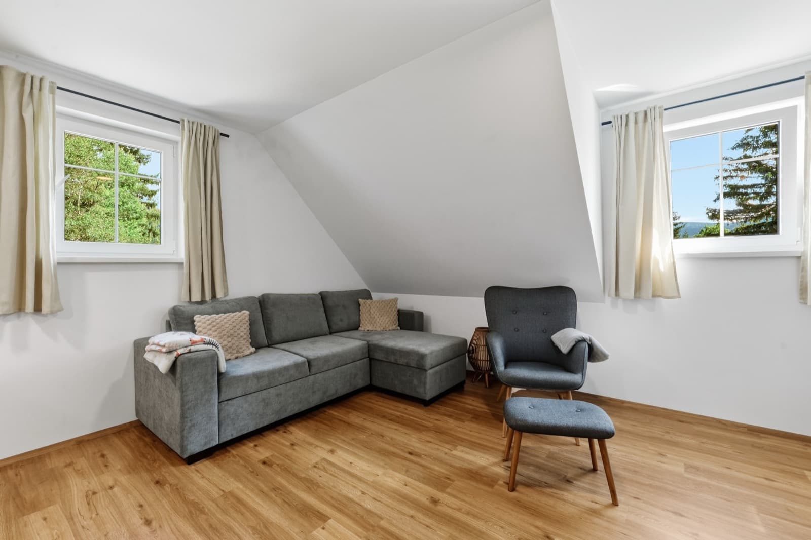 Apartmán Dominik – podkrovní obývací pokoj s rohovou pohovkou, křeslem a okny s výhledem do lesa